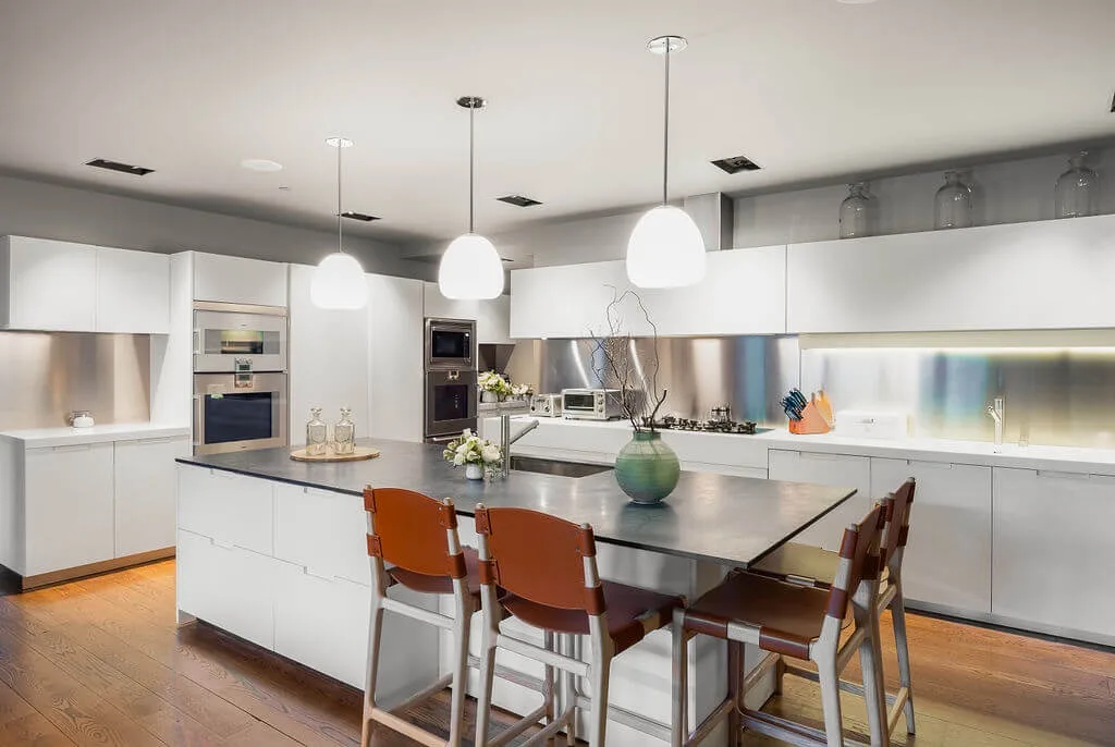 A modern kitchen with a large island, dining seating, and pendant lights.