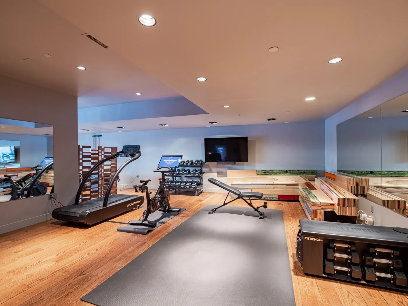 A fitness room with exercise equipment arranged around a large floor mat.