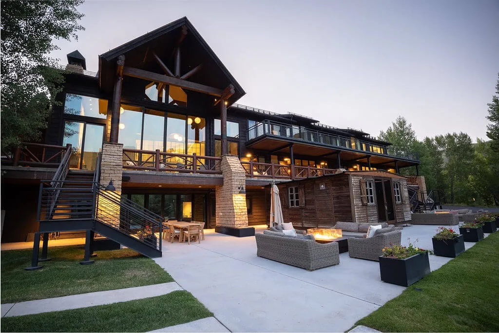 A large timber-and-glass building opens onto a patio with outdoor seating.