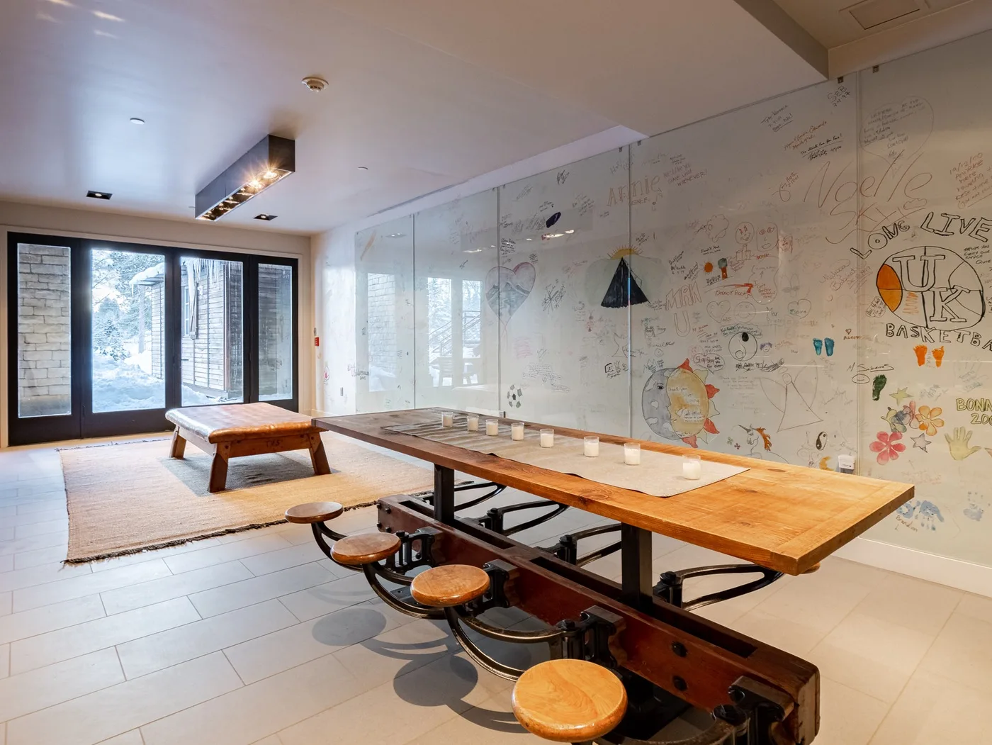 A bright dining area with a long wooden table and wall covered in drawings.