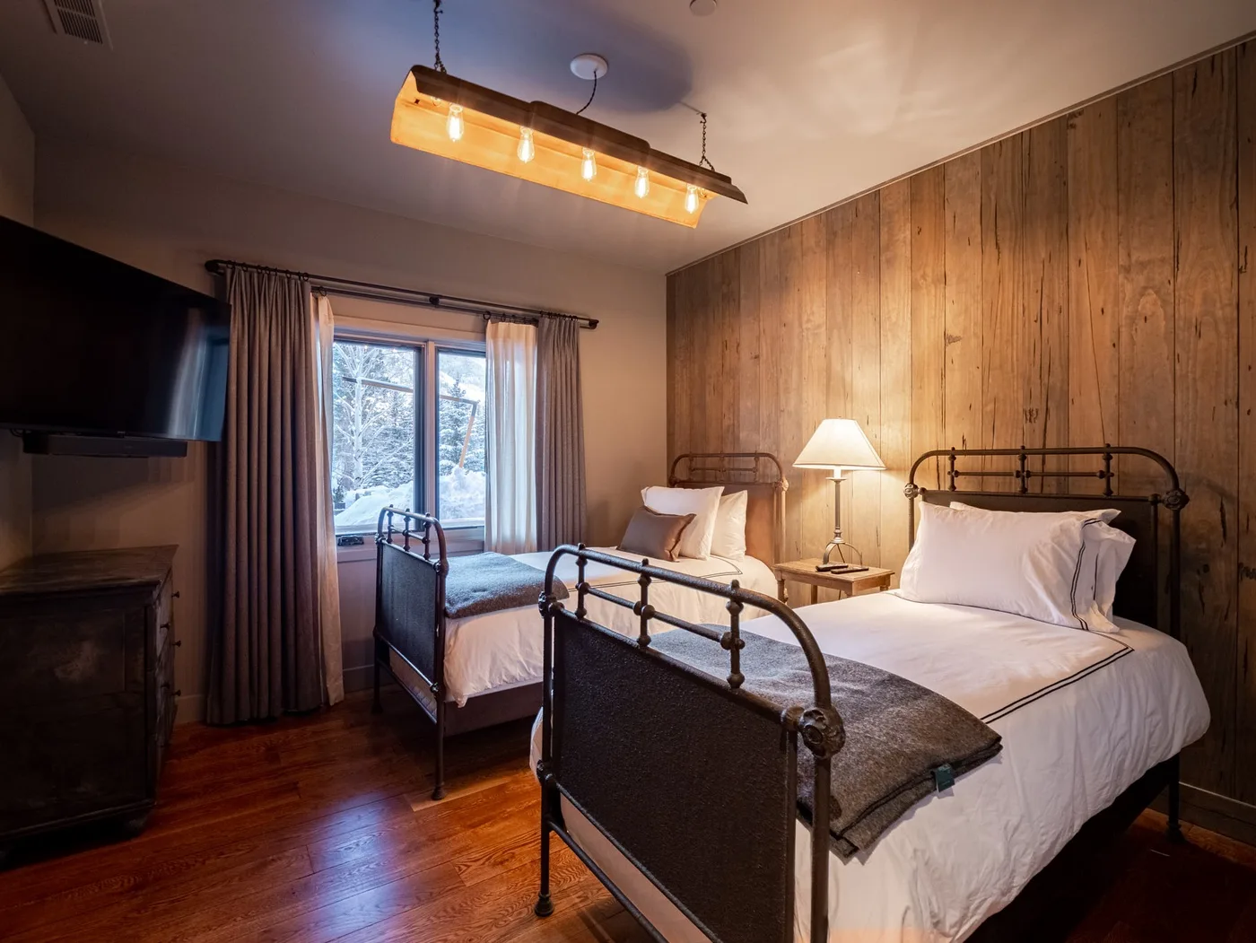 A bedroom with two beds, a bedside lamp, and a window with curtains.