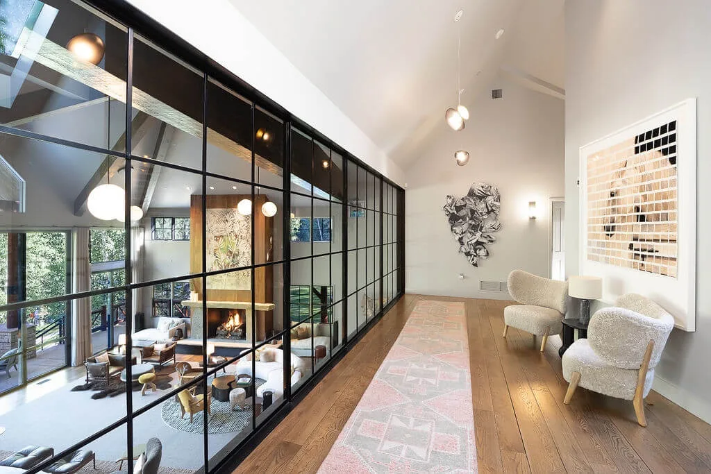 A bright living room with a tall black-framed glass partition and a long patterned rug.