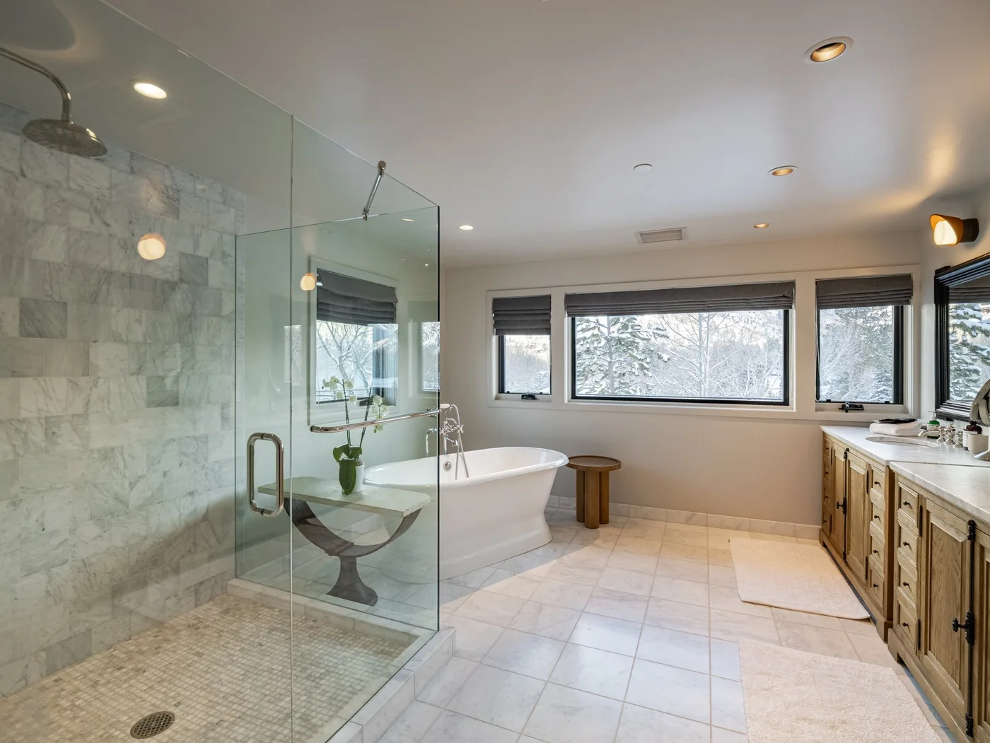 A spacious bathroom with a glass shower, bathtub, and windows.