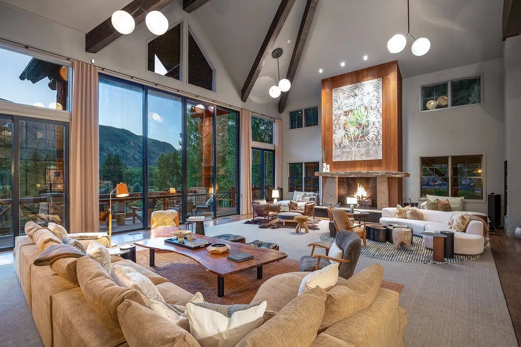 A spacious living room with seating arranged around a fireplace and large windows.