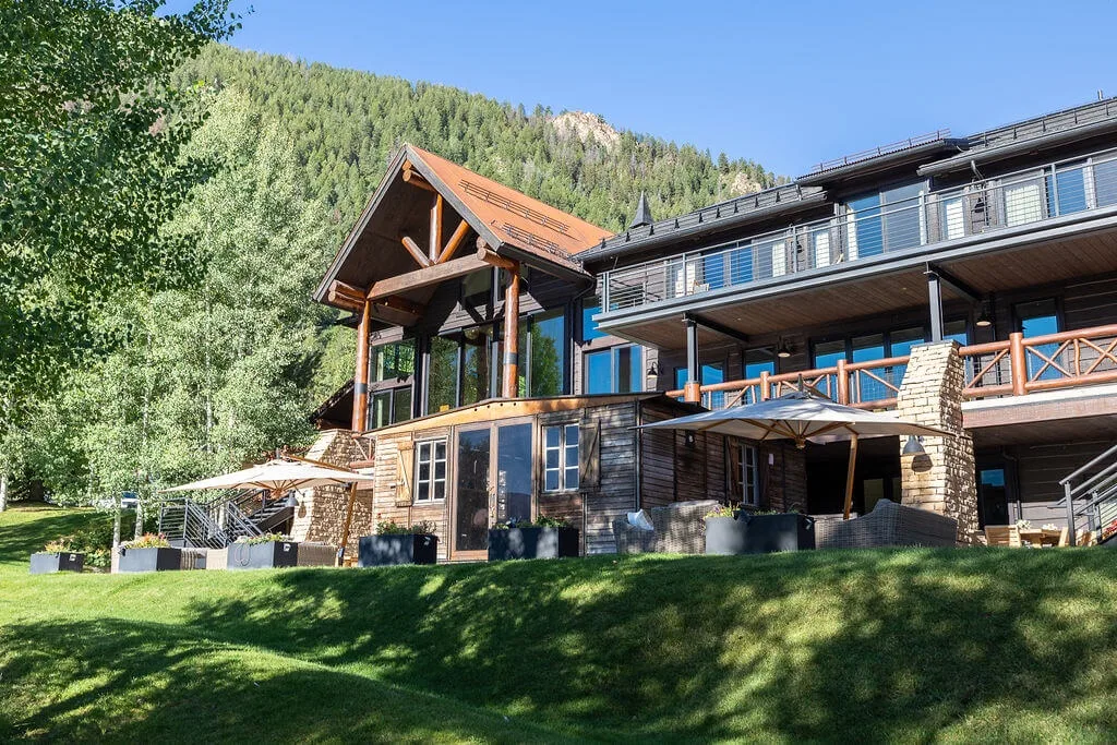 A large lodge-style building with balconies sits beside a wooded hillside.