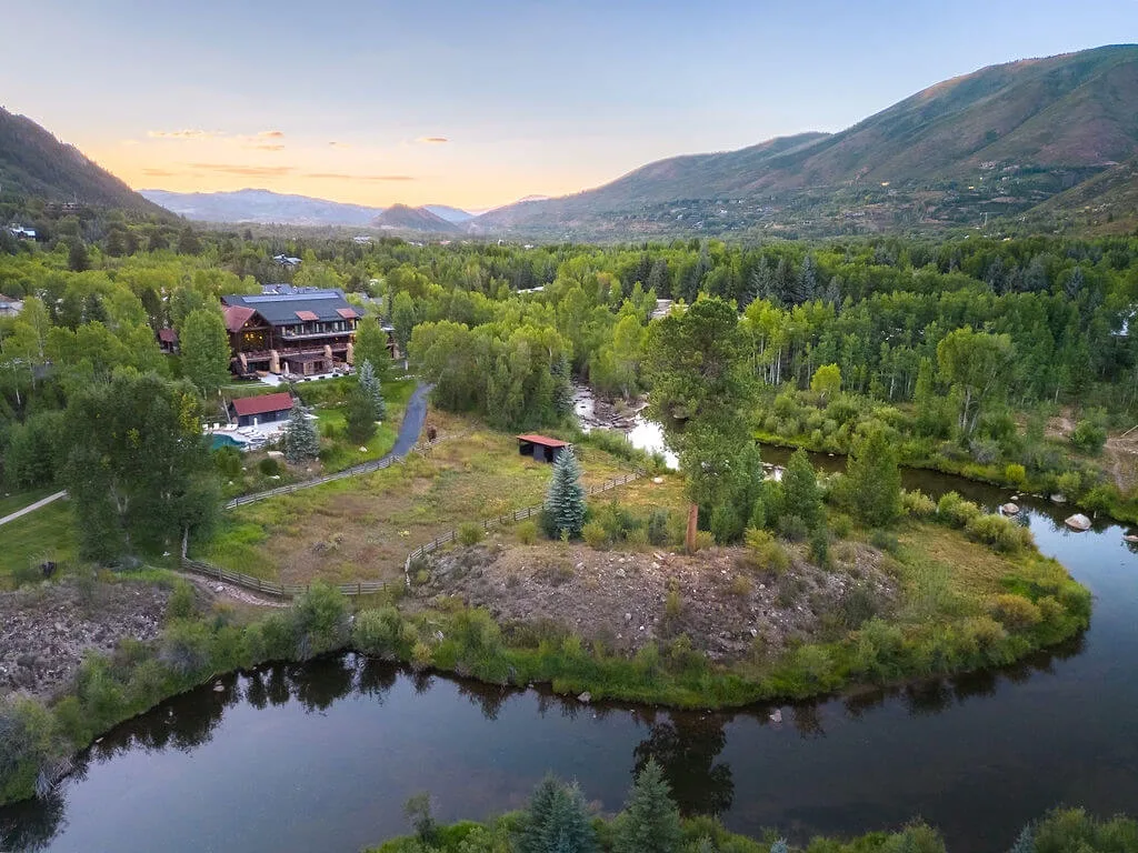 Aerial view of a wooded valley with a river, homes, and mountains.