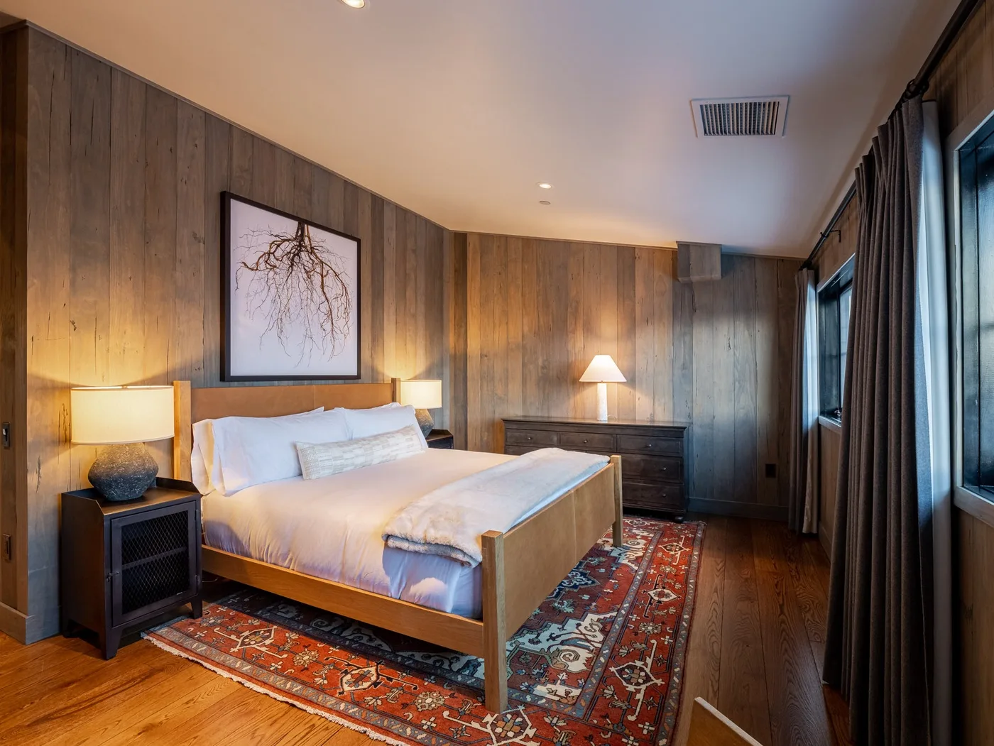 A bedroom with a neatly made bed, bedside tables, and a patterned rug.