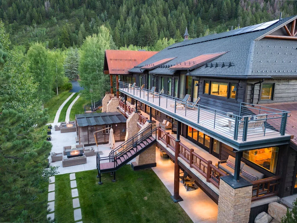 A large lodge overlooks a landscaped yard, with outdoor seating and a winding path.