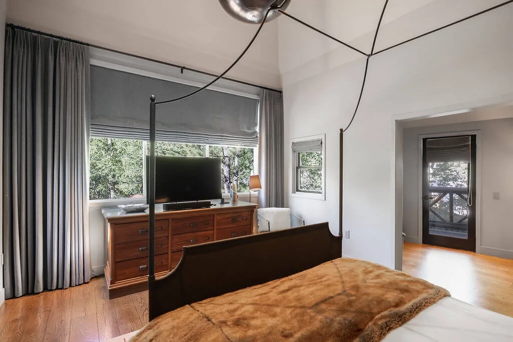 A bedroom with a large bed, a wooden dresser, and a television by the window.