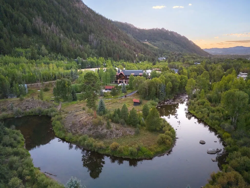 A river bends through a wooded valley, with a few buildings among the trees.