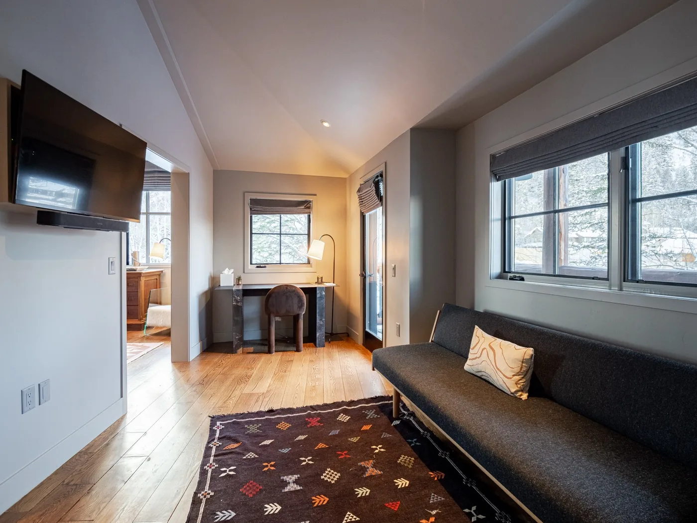 A compact living area with a dark sofa, patterned rug, and desk by the window.