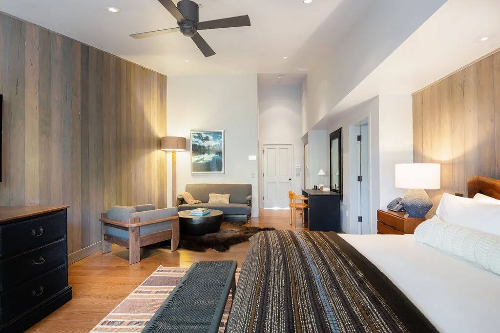 A bright bedroom with a large bed, seating area, and ceiling fan.