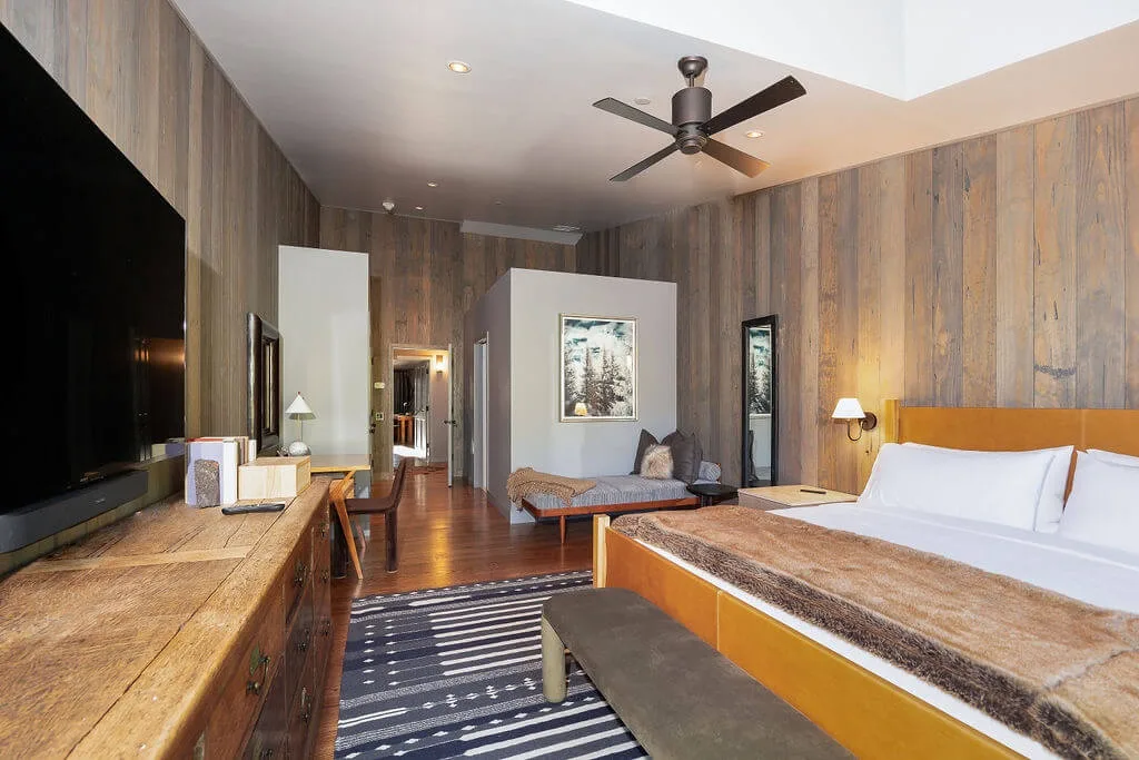 A bedroom with a large bed, wood-paneled walls, and a ceiling fan.