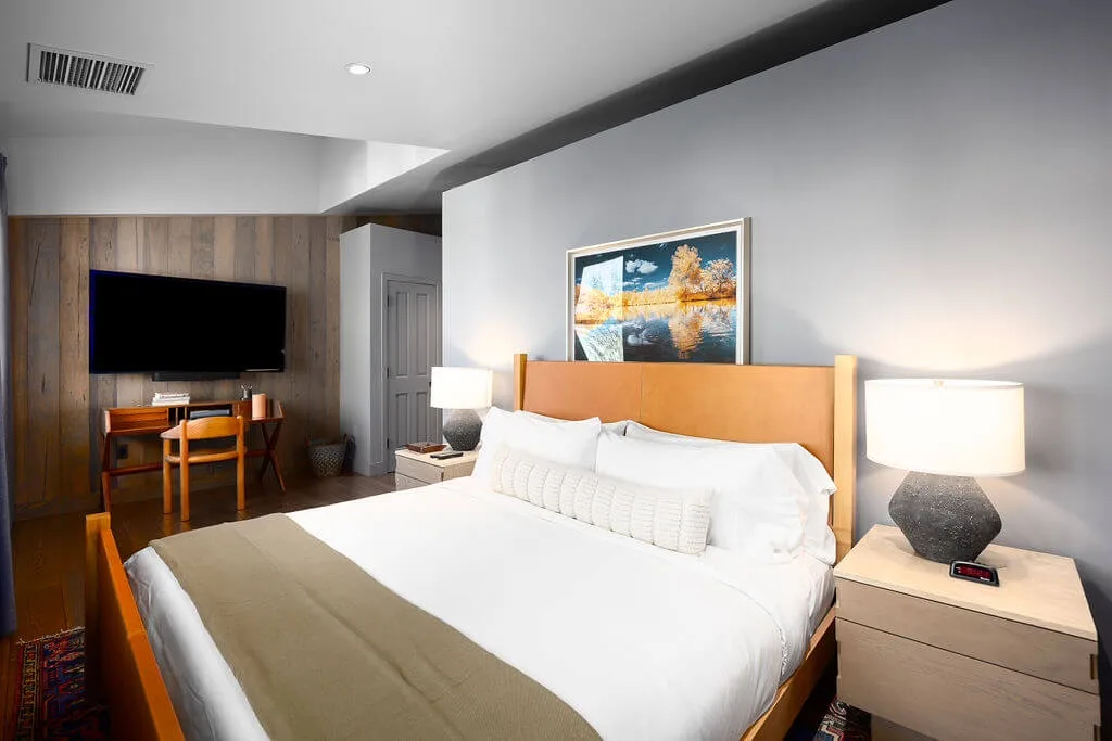 A bedroom with a large bed, bedside lamps, and a television on a wooden wall.