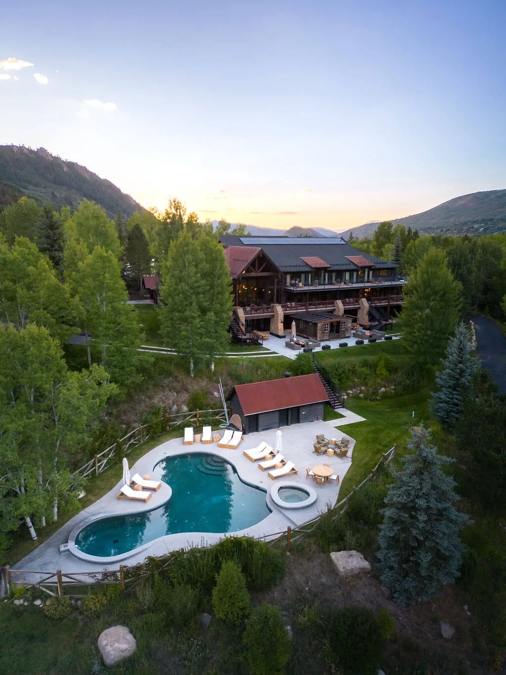 A mountain lodge overlooks a landscaped outdoor pool and seating area.