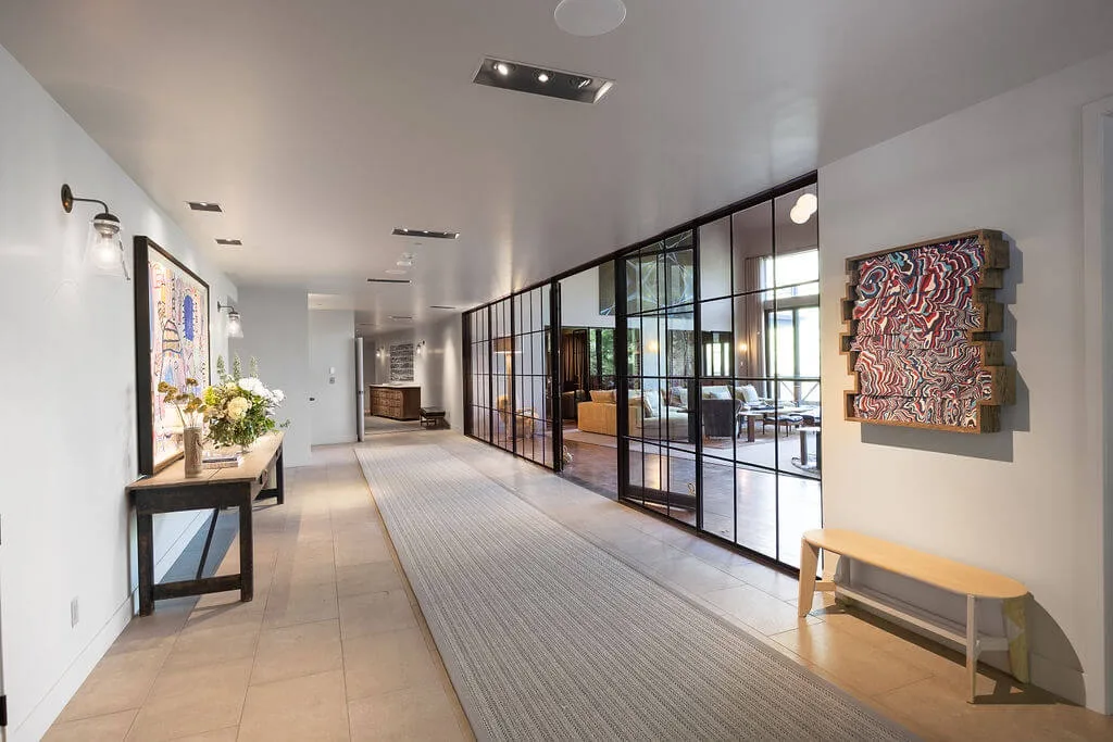 A bright hallway with a long runner beside a glass-partitioned lounge.