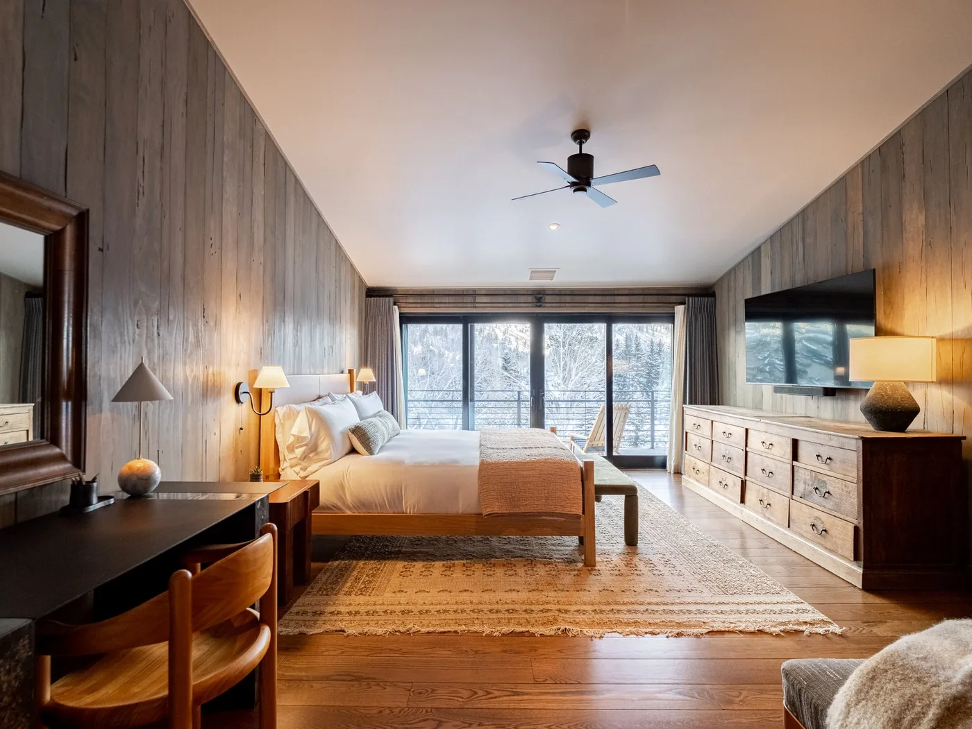 A bedroom with a bed, wooden furnishings, and large windows across the back wall.
