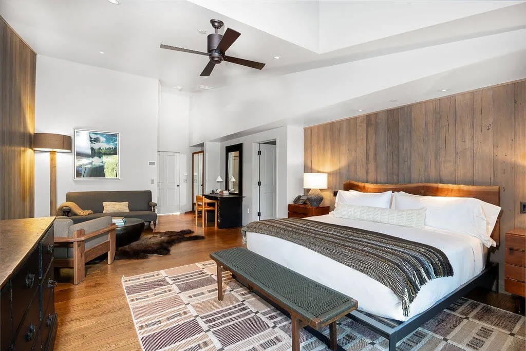 A bright bedroom with a large bed, a seating area, and wood-paneled walls.