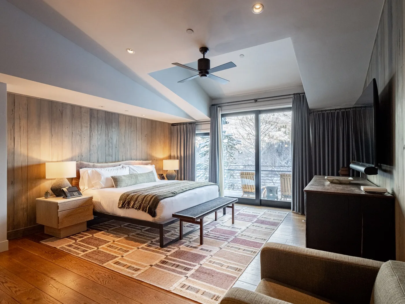 A bedroom with a large bed, patterned rug, and glass doors opening to a balcony.