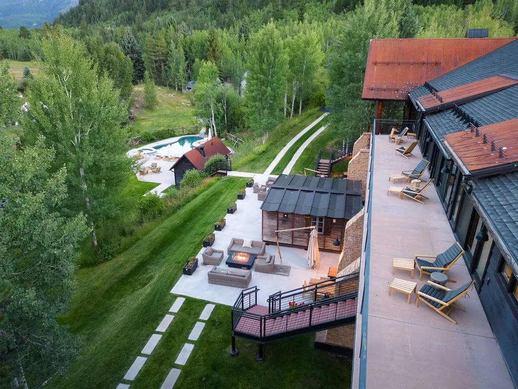 A lodge and outdoor seating areas sit beside a green wooded landscape.