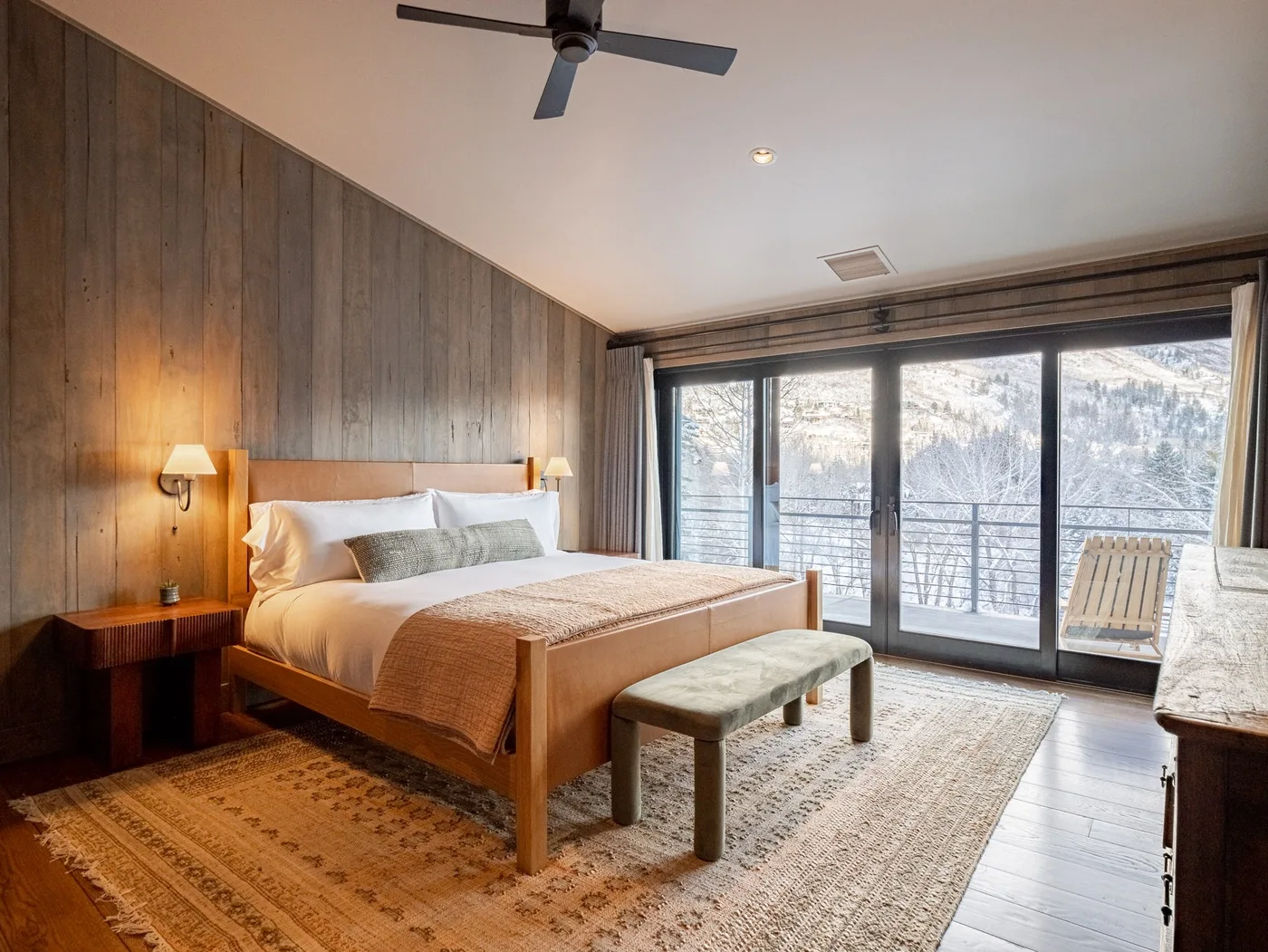 A bedroom with a bed, a bench, and large windows overlooking a snowy landscape.