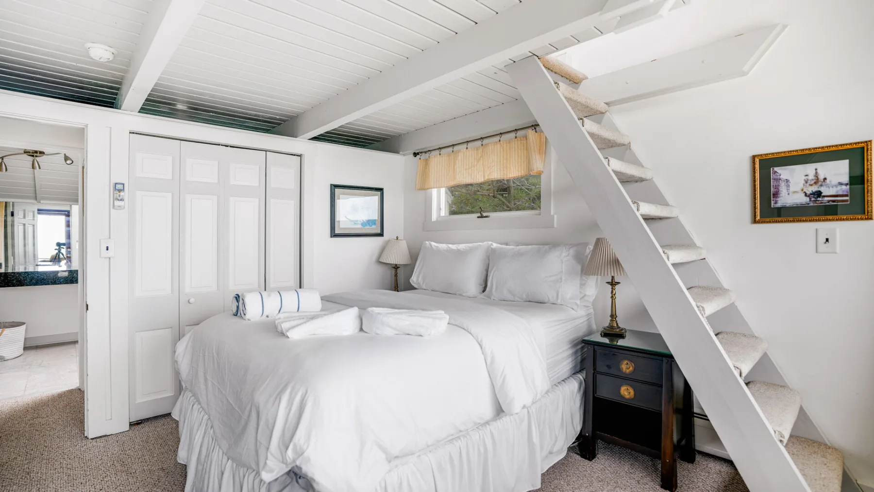 Un dormitorio con una cama blanca debajo de una escalera.