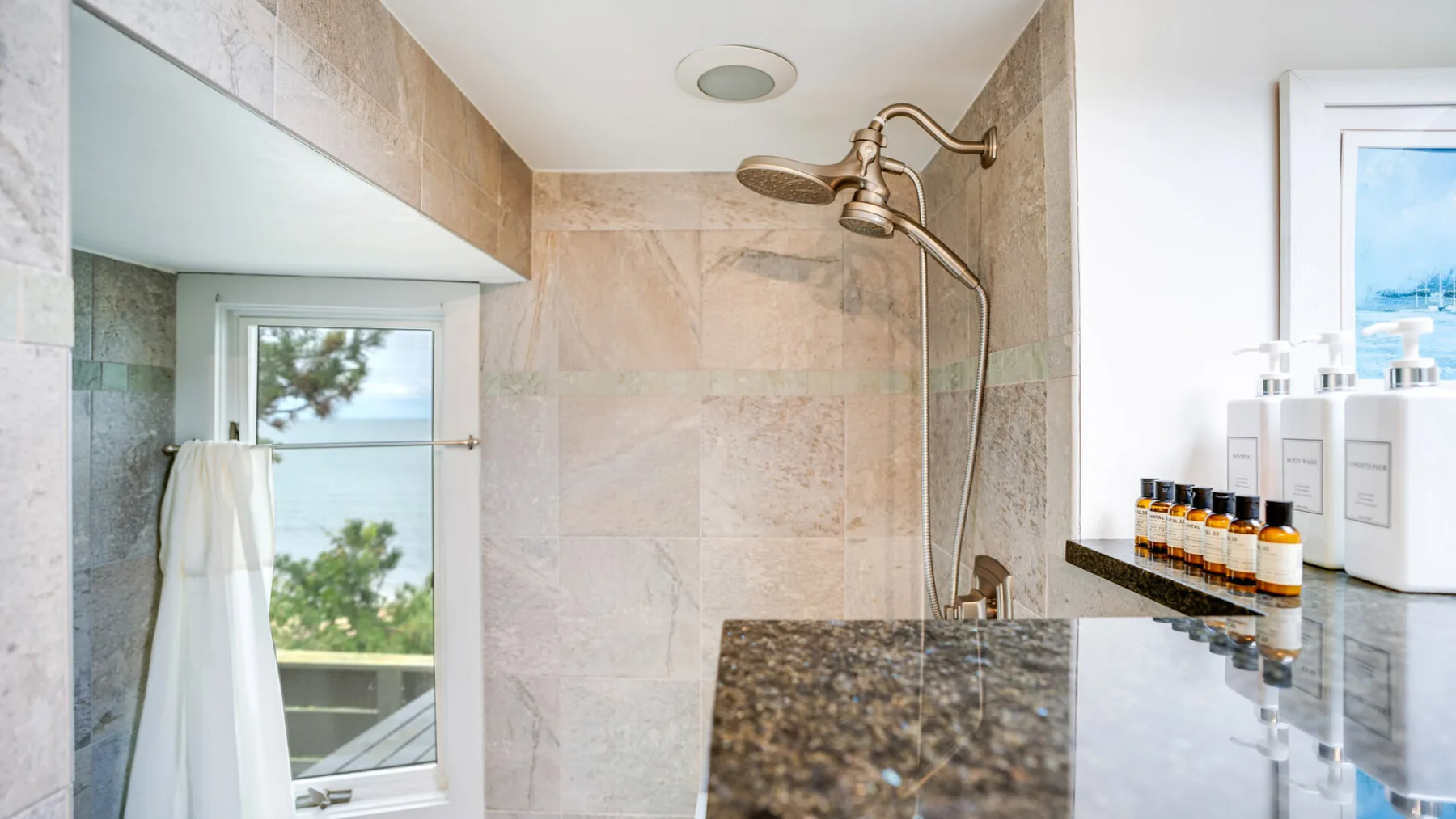 Un baño alicatado con ducha, ventana y artículos de aseo sobre la encimera.
