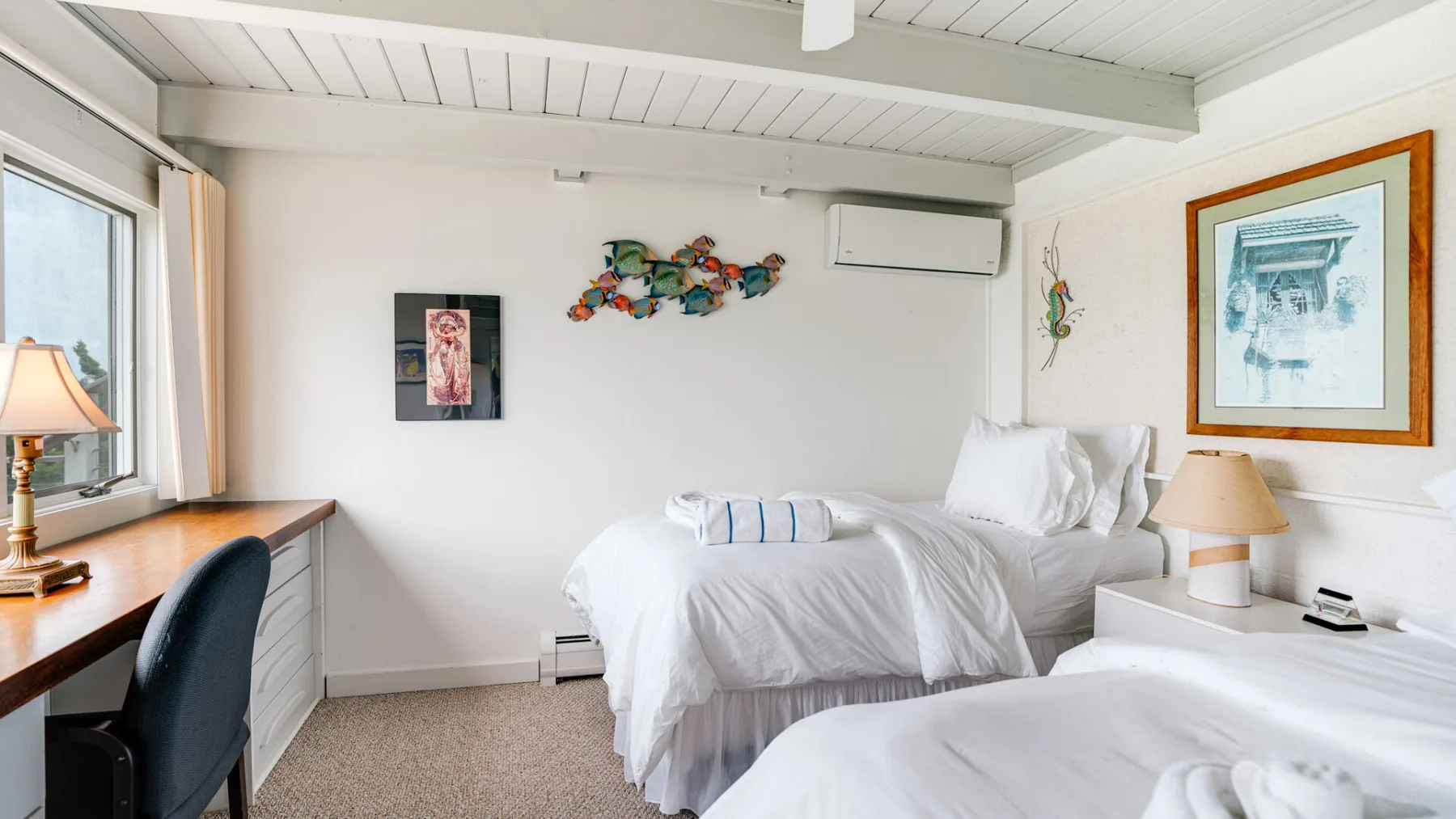 Un dormitorio luminoso con ropa de cama blanca, un escritorio y una ventana.