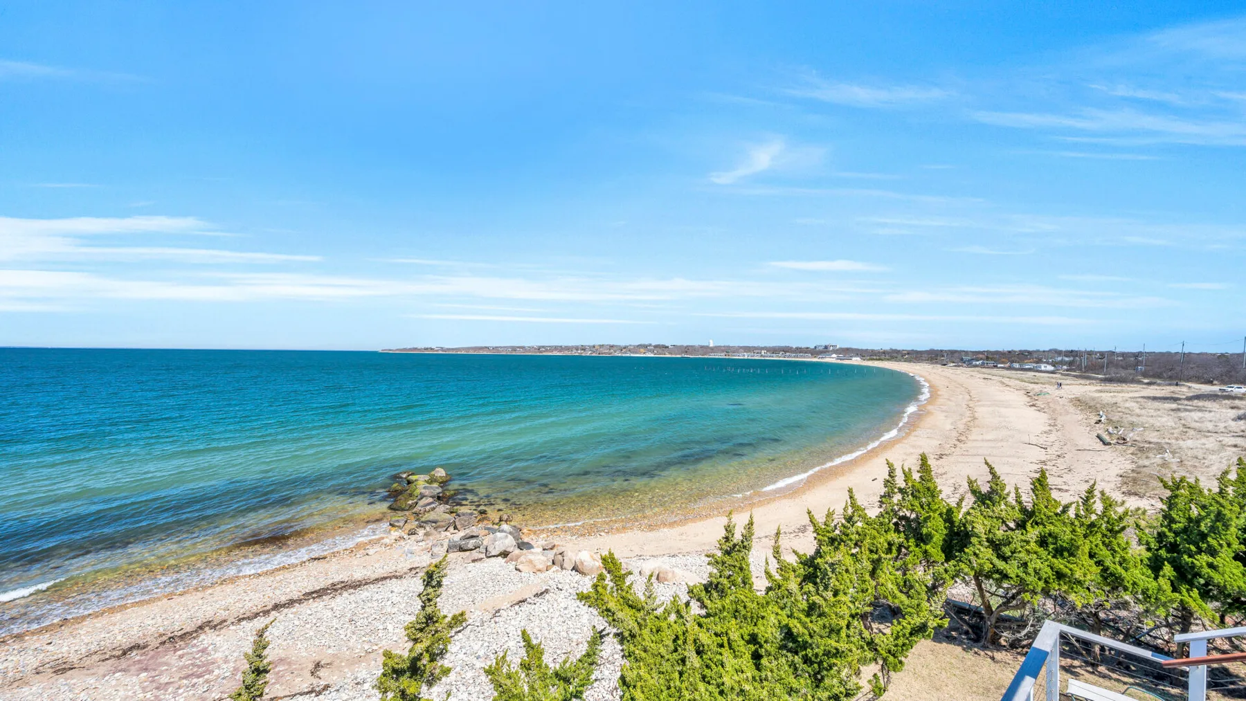 Una playa de arena curva junto a aguas azules y vegetación costera baja.