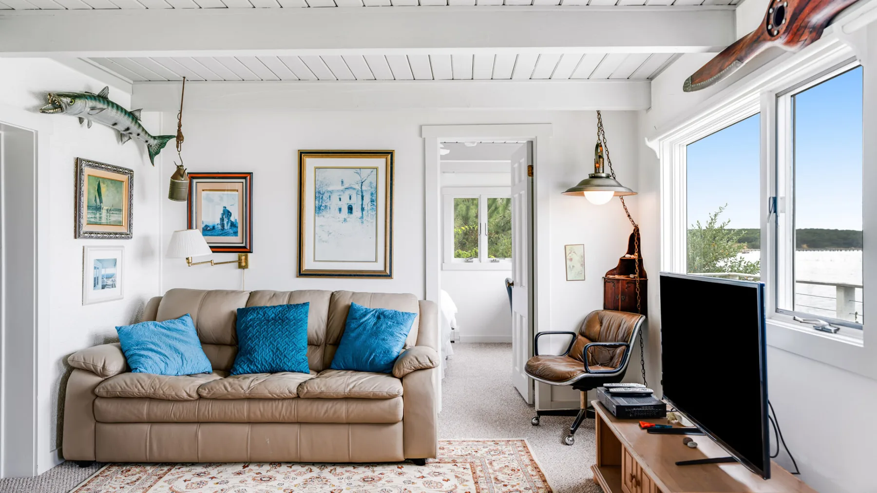 Una sala luminosa con un sofá, cuadros enmarcados y ventanas grandes.