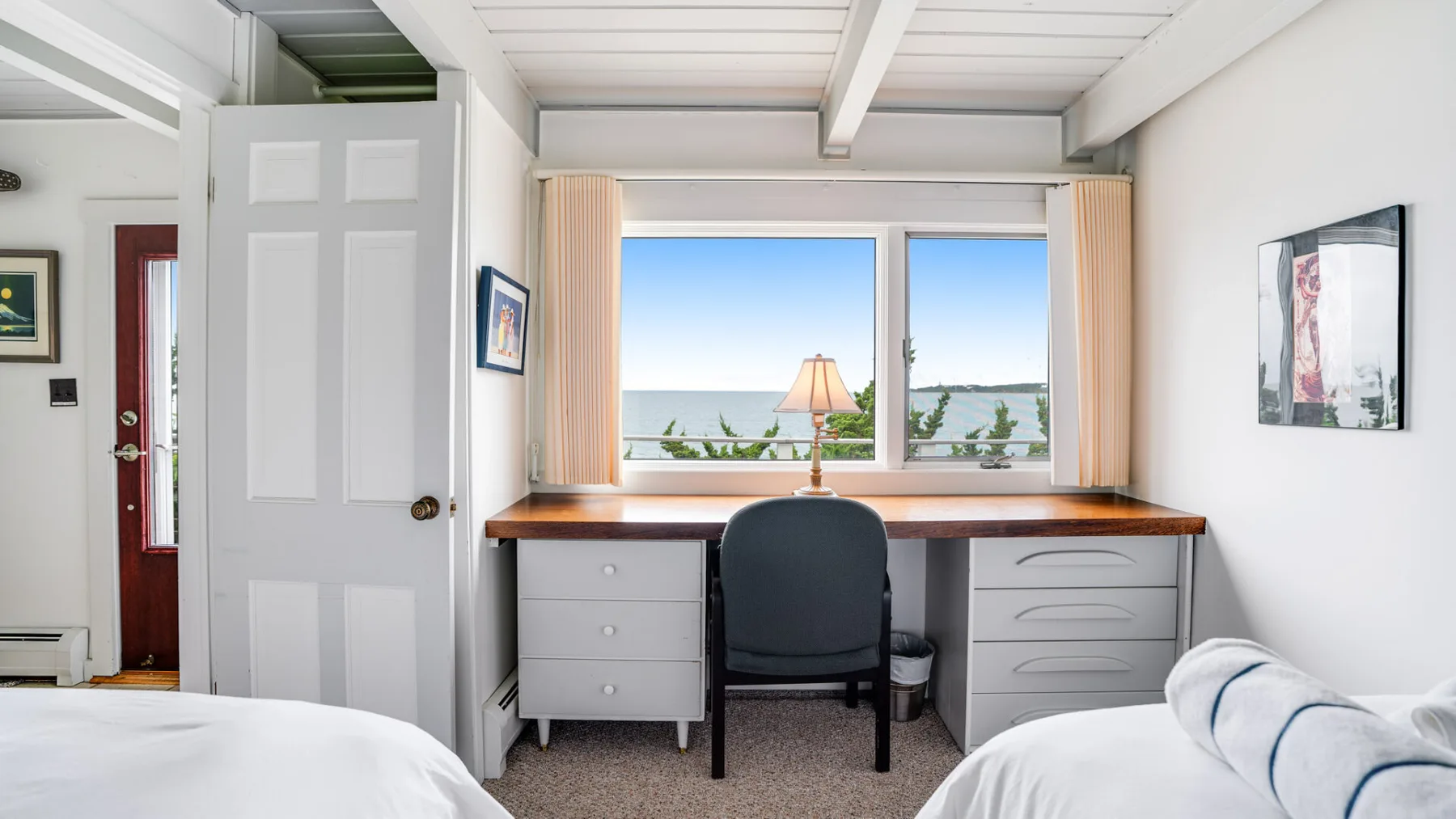 Un dormitorio con un escritorio y una silla frente a amplias ventanas.
