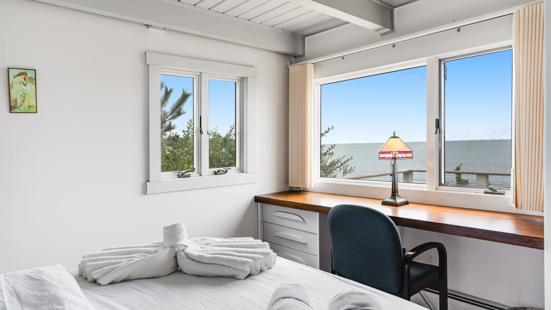 Un dormitorio con una cama, un escritorio y ventanas con vistas al agua.