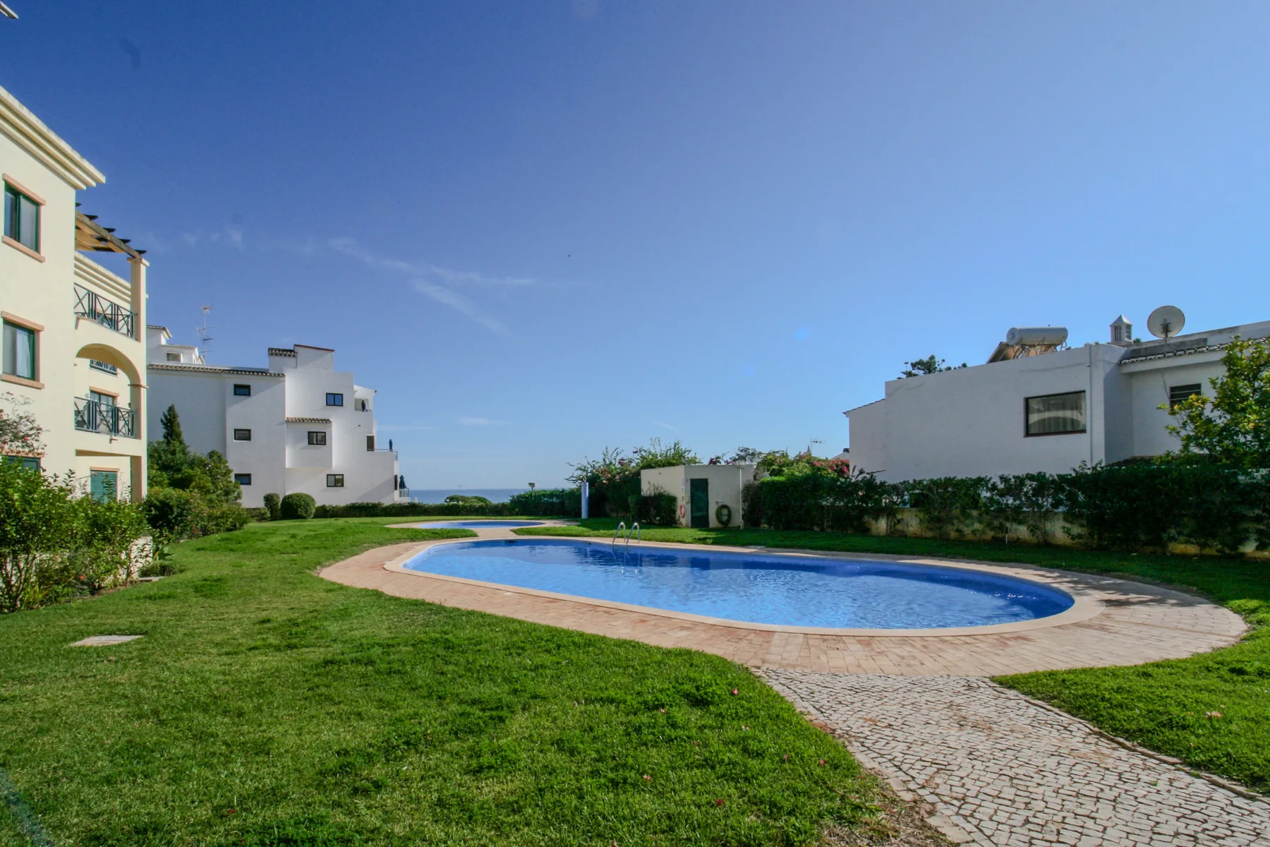 A curved swimming pool sits in a landscaped lawn between apartment buildings.