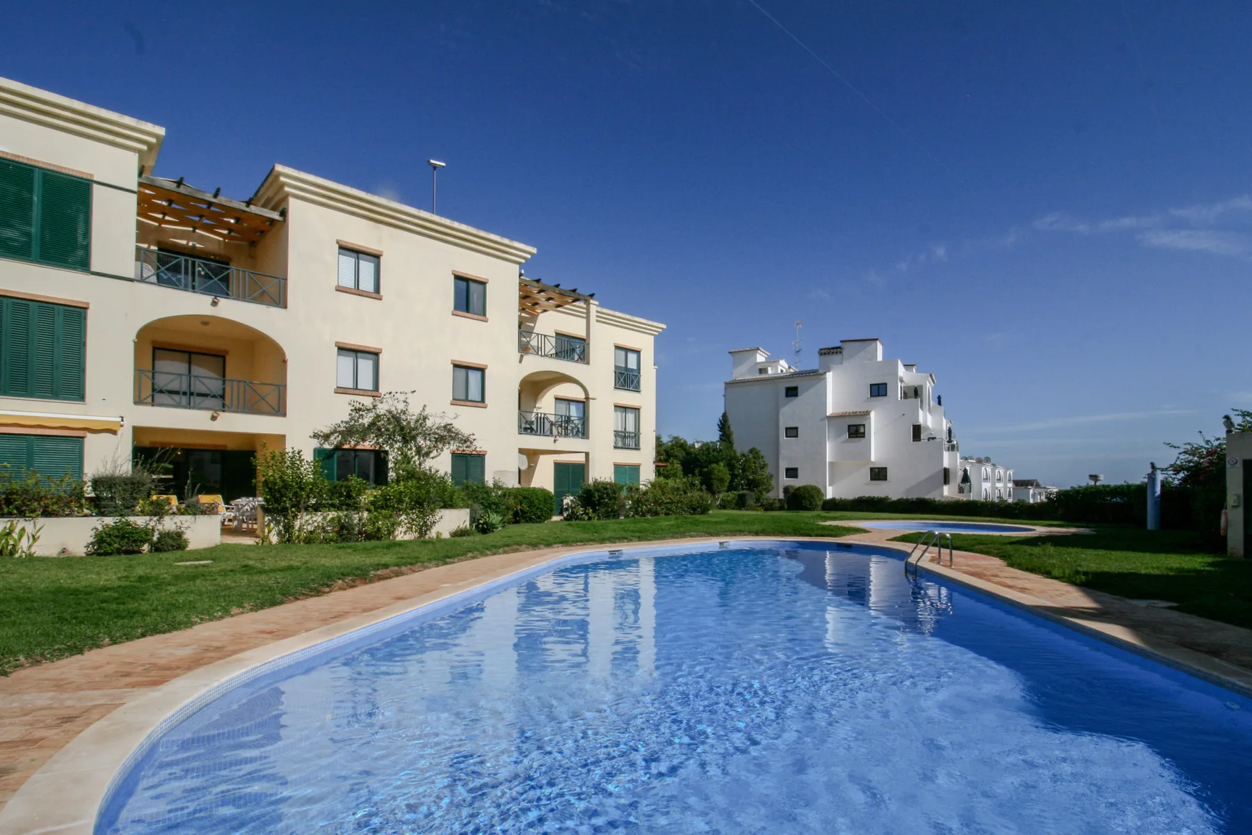 An outdoor swimming pool sits in front of several light-colored apartment buildings.