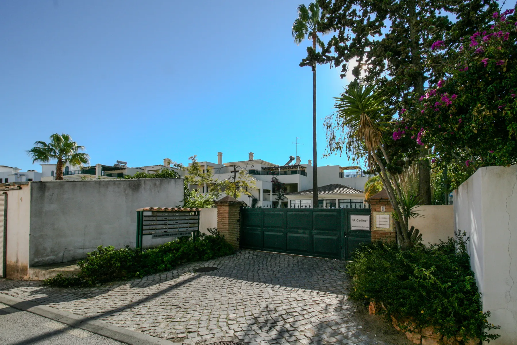 A gated entrance opens onto a cobblestone driveway bordered by greenery.