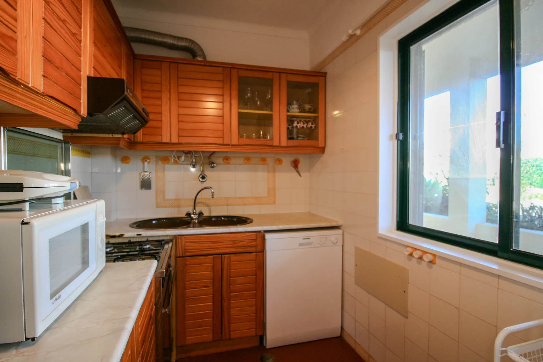 A compact kitchen with wooden cabinets, a stovetop, and a large window.