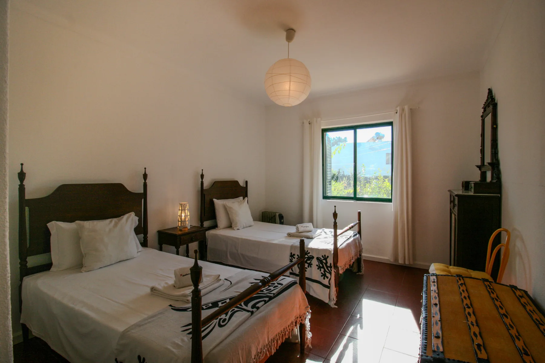 Un dormitorio con dos camas, una ventana y un arcón de madera.