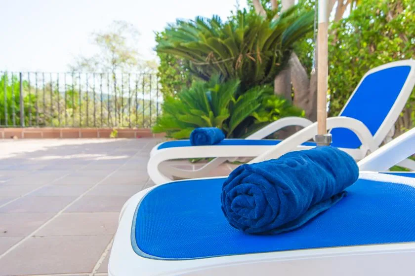 Zona de descanso al aire libre junto a la piscina, con tumbonas azules y plantas frondosas.