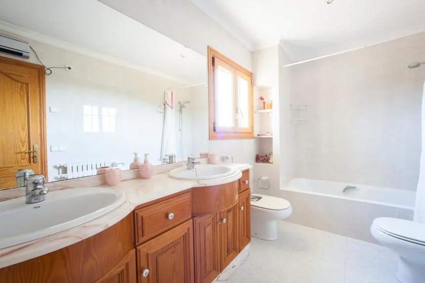 Un baño luminoso con un tocador de madera, lavabos y una bañera.