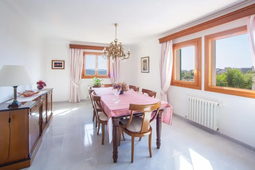 Un comedor luminoso con una mesa larga, sillas y grandes ventanas.