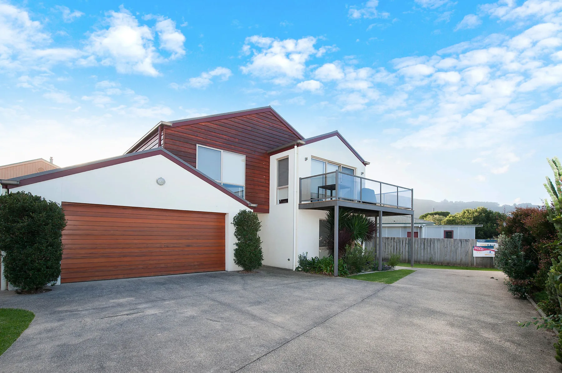 A modern house with a broad driveway, garage, and upper balcony.