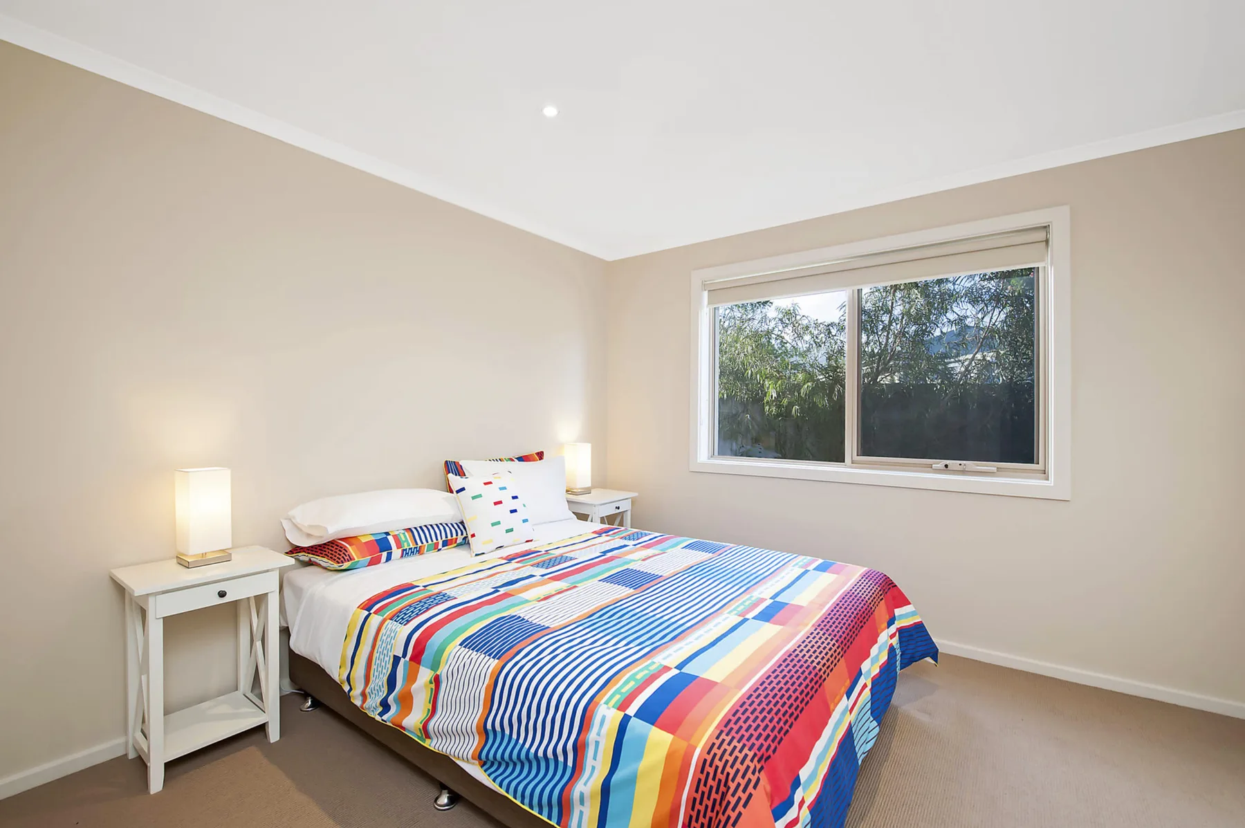 A bedroom with a bed covered in a colorful striped quilt beside a window.