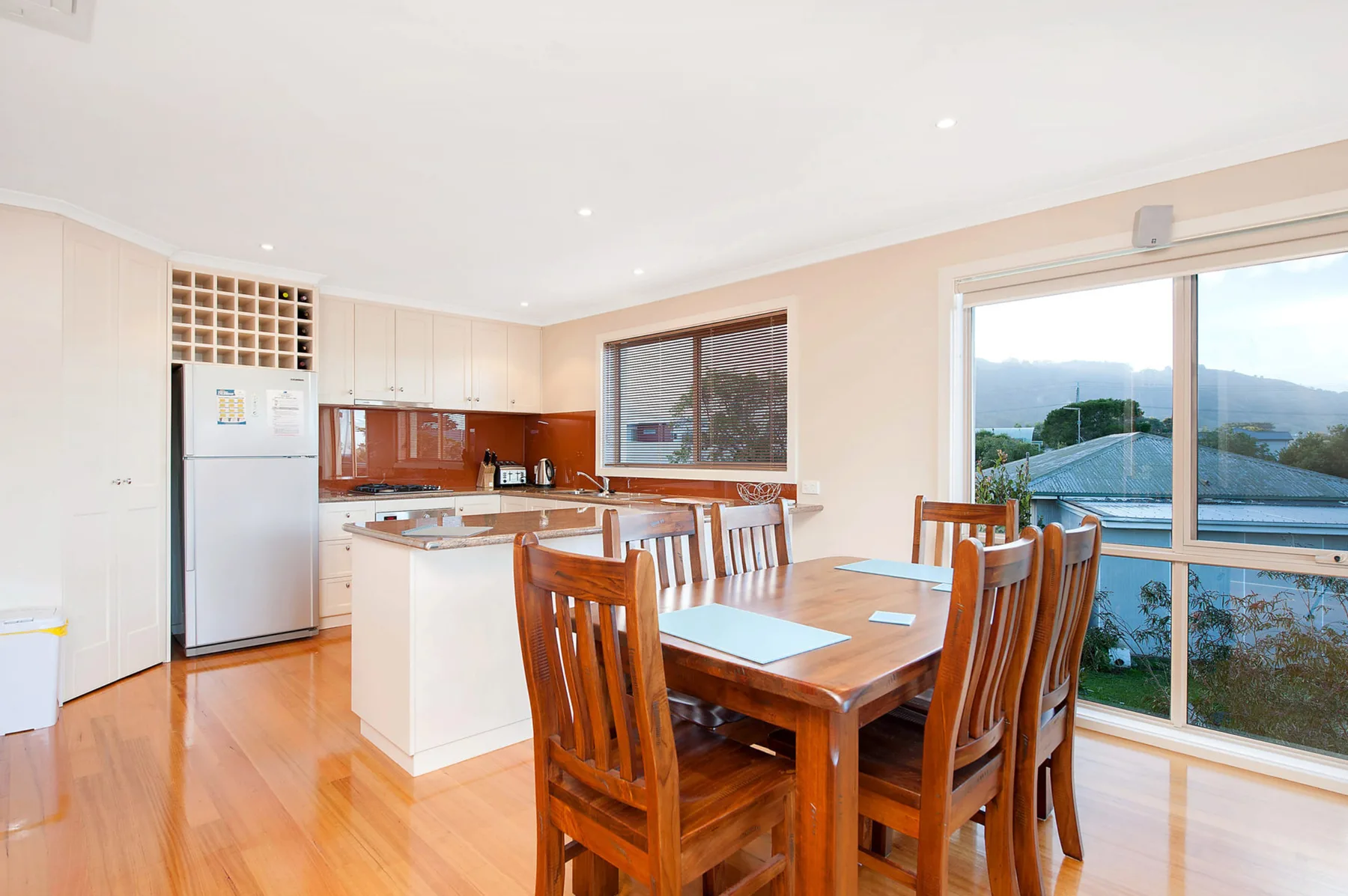 A bright kitchen and dining area with wooden seating beside large windows.