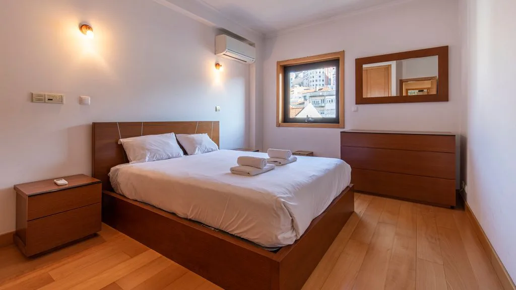 A bedroom with a neatly made bed, wooden furnishings, and a framed picture.
