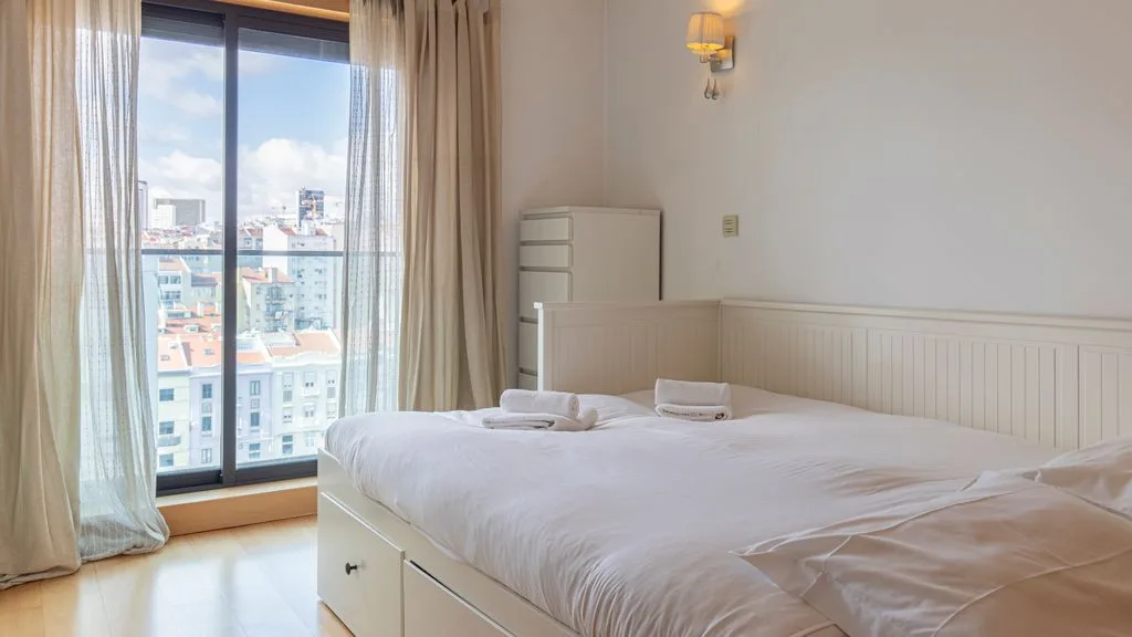 A bedroom with a neatly made bed beside a large window.