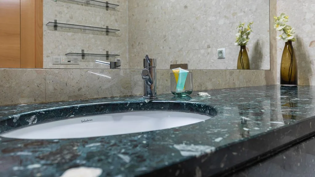 A bathroom vanity with a wide sink, wall mirror, and small flower arrangements.