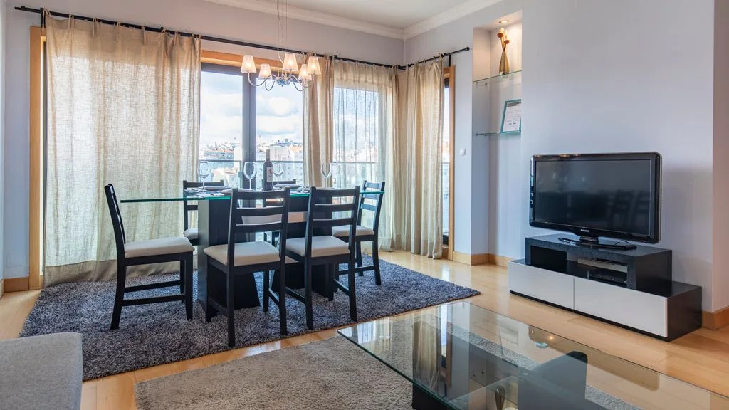 A dining and living area with a glass table, seating, and a television.