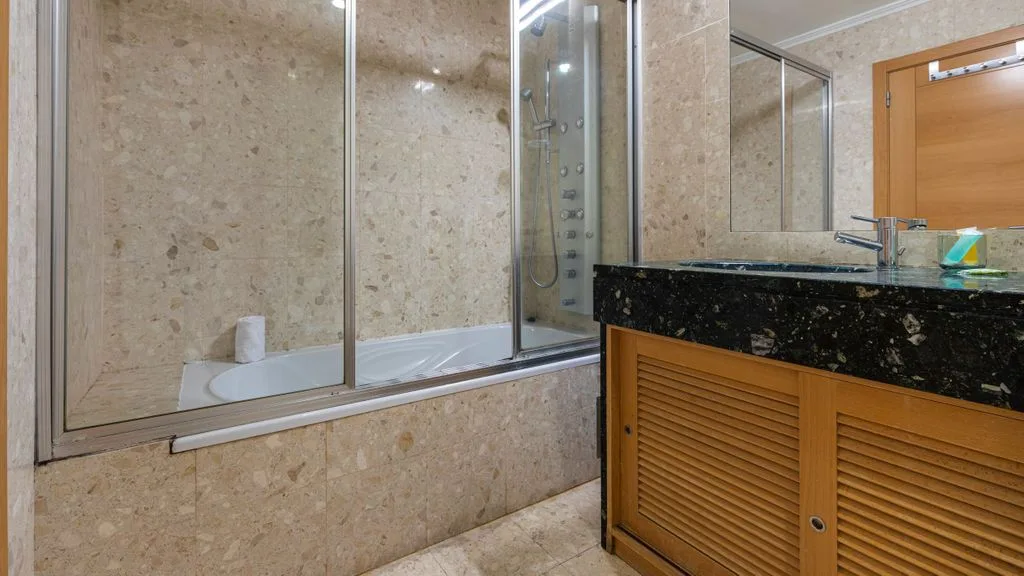 A bathroom with a bathtub behind glass panels and a wood vanity.