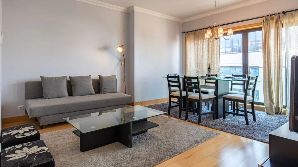 A living and dining area with seating, a glass coffee table, and a table by the window.