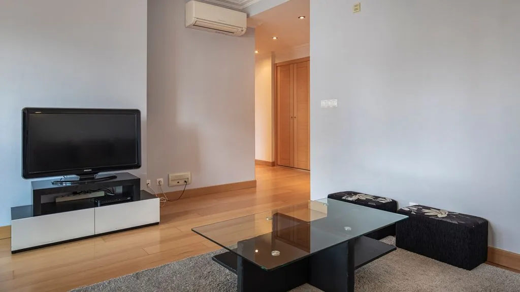 A living room with a television, glass coffee table, and seating.